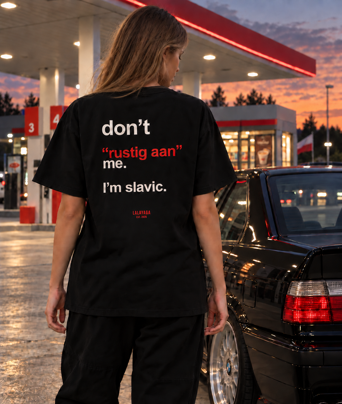 Modelka w czarnej koszulce LALAYAGA don’t rustig aan me. I’m slavic. i czarnych spodniach przy BMW